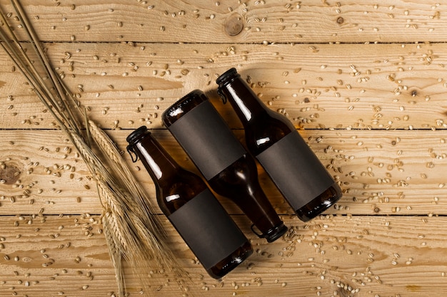 Top view of three beer bottles and ears of wheat on wooden plank