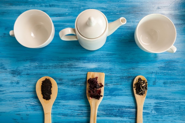 Top view of three cups for tea on vintage blue wooden background next to three spoons of tea leaves