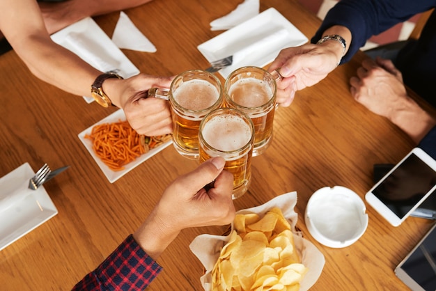 Free photo top view of three unrecognizable friends toasting with beer mugs