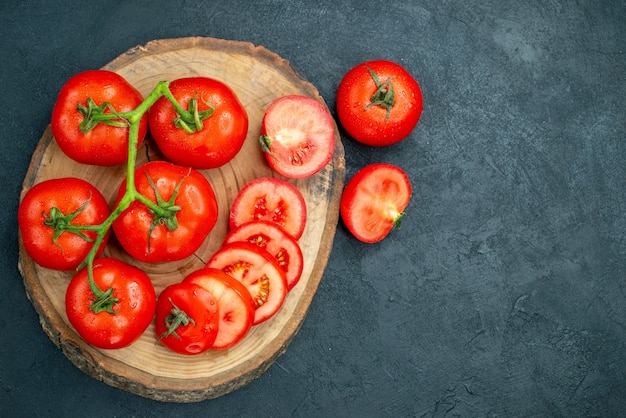 Top view tomato branch on woodserving board chopped tomatoes dark background