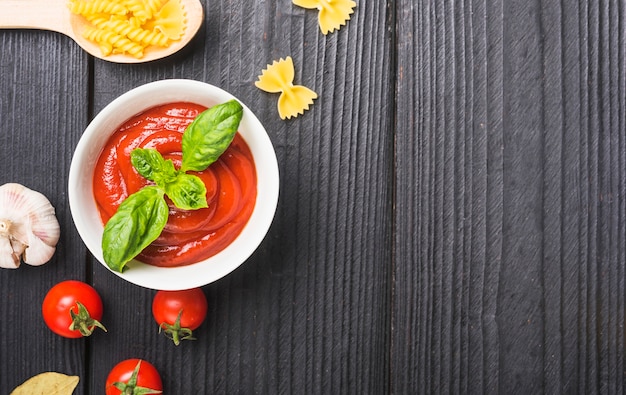 Top view of tomato sauce with garlic and pasta on wooden plank