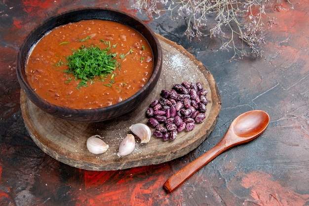 Free photo top view of tomato soup beans garlic on wooden cutting board and spoon on mix color background