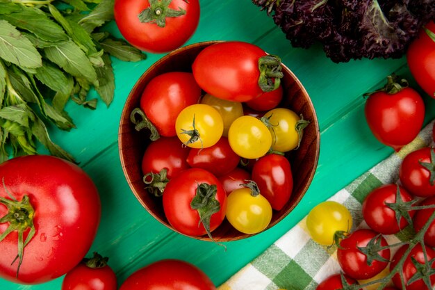 Top view of tomatoes in bowl with green mint leaves and basil on green surface