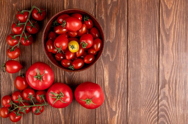 Top view of tomatoes in bowl with other ones on left side and wood with copy space