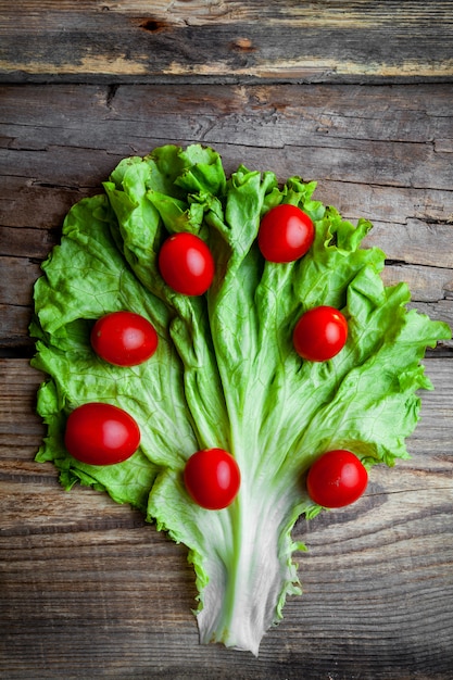 Free photo top view tomatoes on lettuce on dark wooden background. vertical