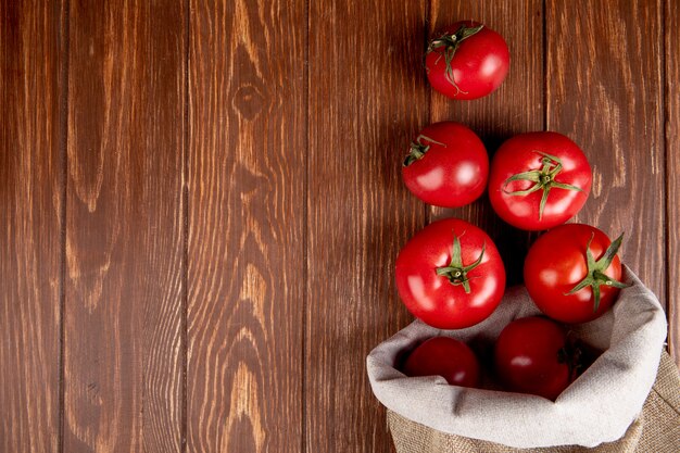 Top view of tomatoes spilling out of sack on right side and wooden surface with copy space