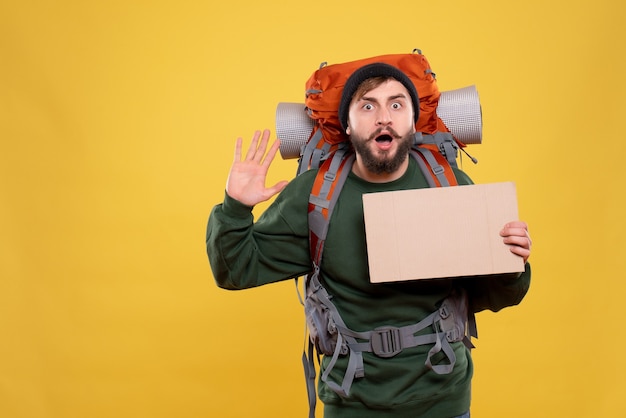 Free photo top view of travel concept with shocked young guy with packpack and holding free space for writing showing five