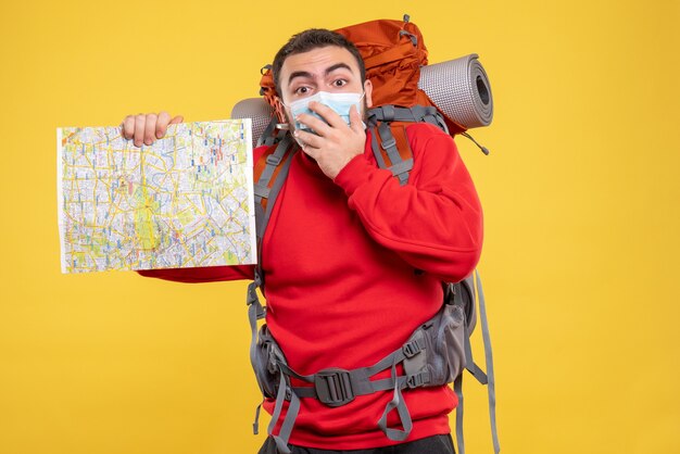 Top view of a traveller guy wearing medical mask with backpack holding map on yellow background