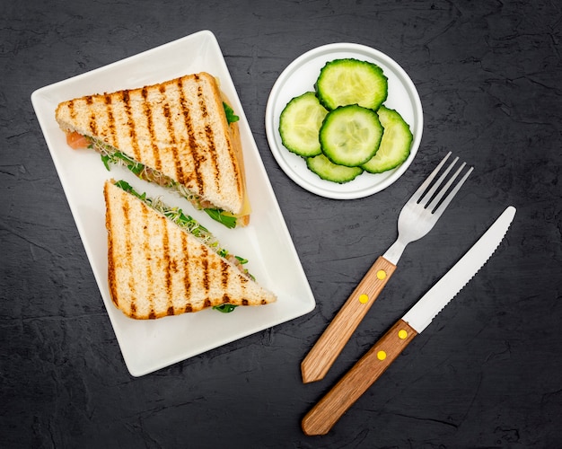 Top view of triangular sandwiches on plate with cutlery and cucumber slices