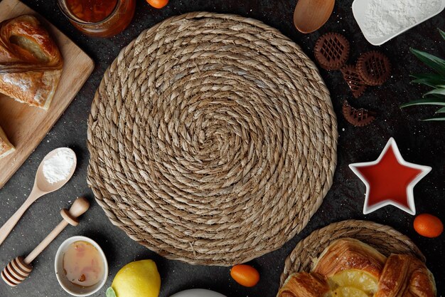 Top view of trivet for hot dishes with flour jam lemon kumquats croissant cookies on black background