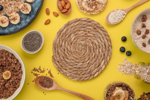 Top view of trivet with banana blackthorn oatmeal banana crispbread snack banana walnut and walnut milk oatmeals and banana smoothie with chia seeds spoons full of almond flax on yellow background