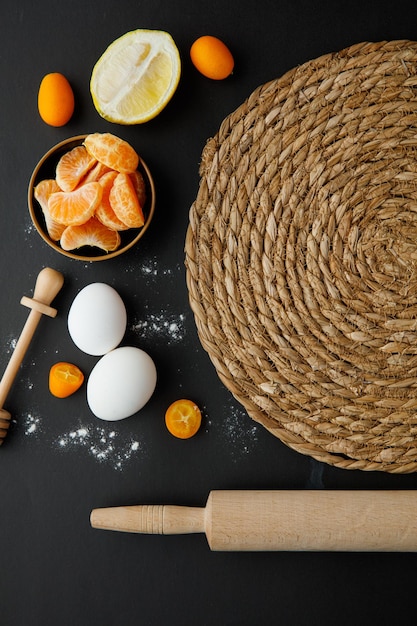 Top view of trivet with egg lemon half tangerine slices kumquat with honey dipper and rolling pin on black background