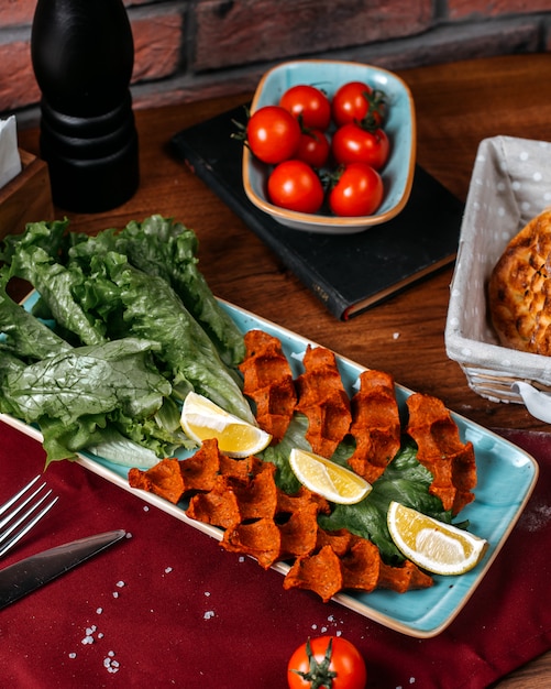 Top view of turkish food cig kofte with lemon and lettuce on a wooden table