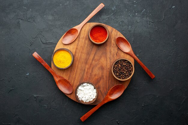 Top view turmeric red pepper black peper sea salt in smal bowls four spoons on round board on dark table with copy space