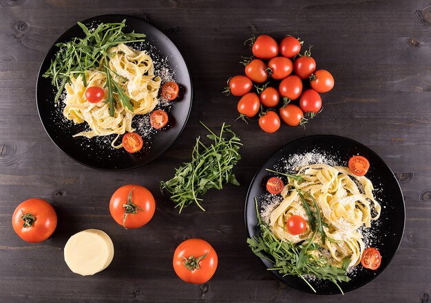 Free photo top view of two black plates with tagliatelle pasta on wooden table