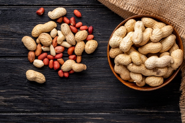 top view unshelled peanuts in a bowl with peeled on a black wooden table