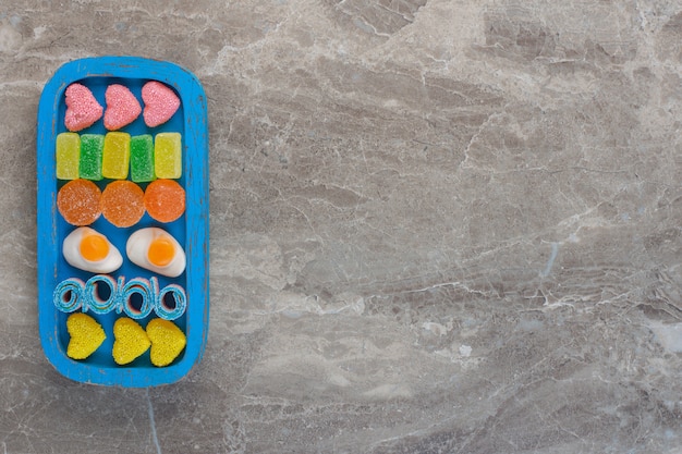 Free photo top view of various candies on blue wooden plate over grey background.