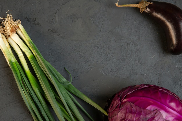 Top view of various fresh vegetables red cabbage eggplant and green onion with copy space on dark j