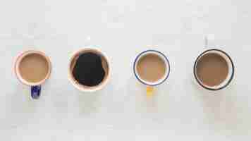 Free photo top view of various kinds of coffee in cups arranged in a row over white wooden desk