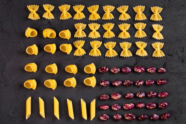 Top view of various raw pasta with kidney beans arranged on black