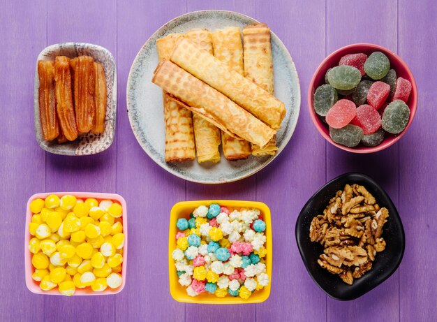 Top view of various sweets for tea candies marmalade walnuts and pastries on purple wooden background