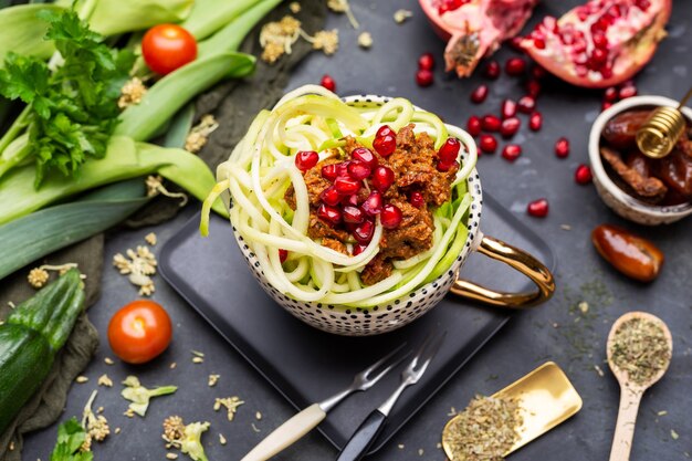 Top view of a vegan meal with spiralized zucchini, tomato sauce and pomegranates in the cup