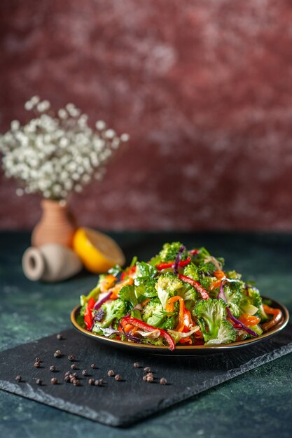 Top view of vegan salad with fresh ingredients in a plate and pepper on black cutting board