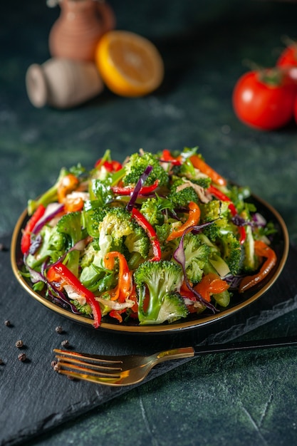 Top view of vegan salad with fresh ingredients in a plate and pepper on black cutting board