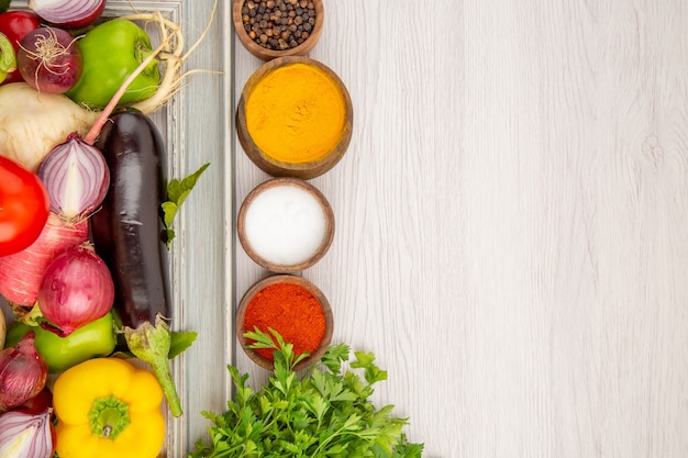 Top view vegetable composition with seasonings and greens on white table