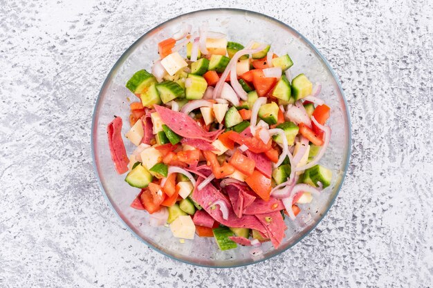 Top view vegetable salad chopped in glass bowl with tomato onion cucumber on white stone