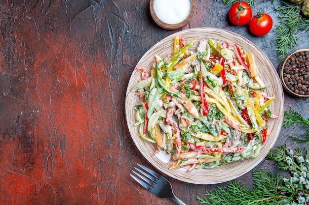 Free Photo top view vegetable salad on plate fork tomatoes salt black pepper pine branches on dark red table copy space