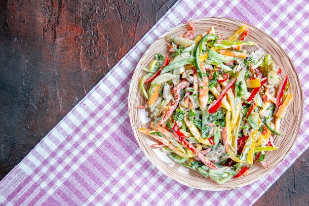 Top view vegetable salad on plate on tablecloth on dark red table free place