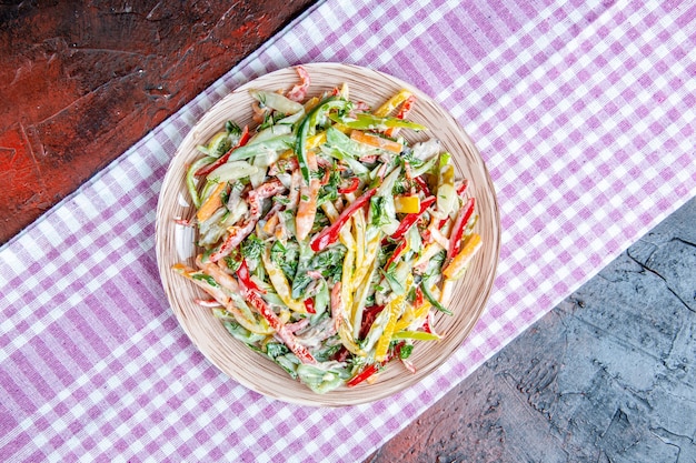 Top view vegetable salad on plate on tablecloth on dark red table