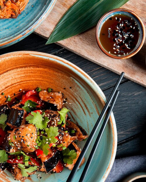 Top view of vegetable salad with fried eggplant tomatoes herbs and sesame in a bowl served with soy sauce on wood