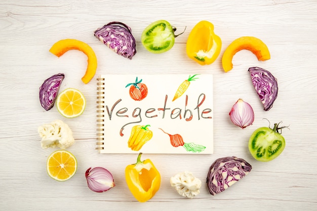 Free Photo top view vegetable written on notepad cut vegetables red cabbage green tomato pumpkin red onion yellow bell pepper caulifower lemon on white table