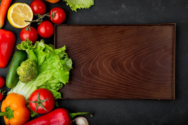 Top view of vegetables as broccoli lettuce tomato cucumber with lemon and cutting board on black background