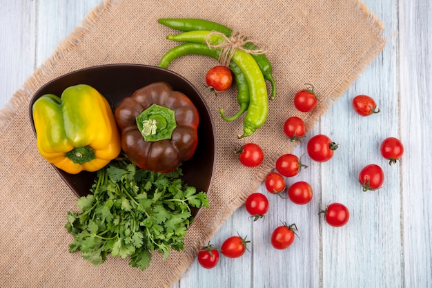 Top view of vegetables as bunch of coriander pepper in bowl and on sackcloth with tomatoes on wooden surface