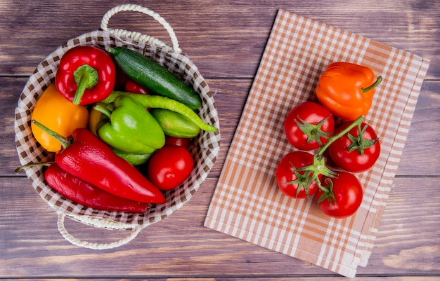 Free photo top view of vegetables as cucumber pepper tomato in basket with tomatoes and pepper on plaid cloth and wood