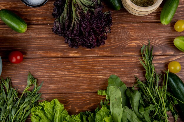 Top view of vegetables as cucumber tomato basil mint lettuce spinach with black pepper salt on wood