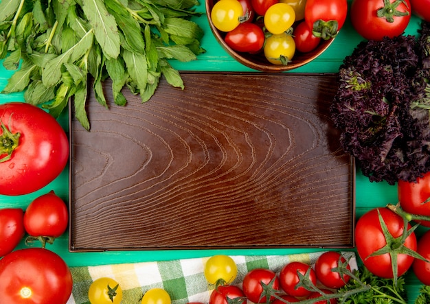 Top view of vegetables as green mint leaves basil tomato around empty tray on green