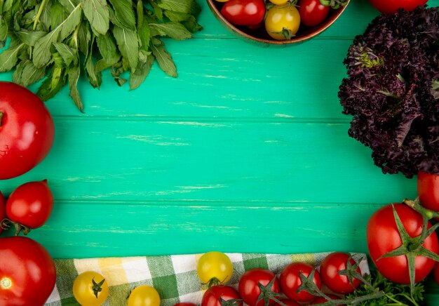 Top view of vegetables as green mint leaves tomato basil on green surface with copy space