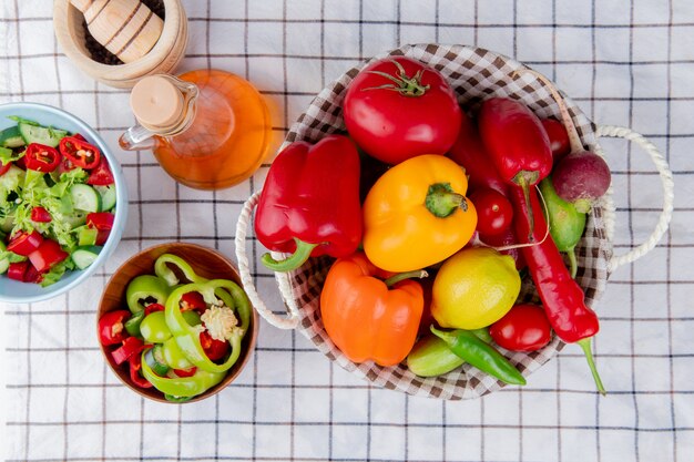 Top view of vegetables as pepper tomato cucumber in basket with vegetable salad melted butter and garlic crusher on plaid cloth