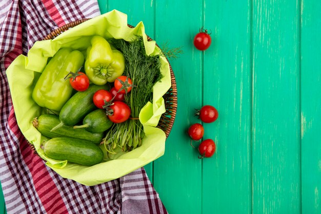 Top view of vegetables as pepper tomato cucumber dill in basket on plaid cloth and green surface