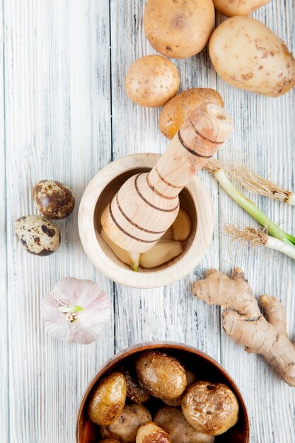 Top view of vegetables as potato egg garlic ginger with baked potato and garlic crusher on wooden background with copy space