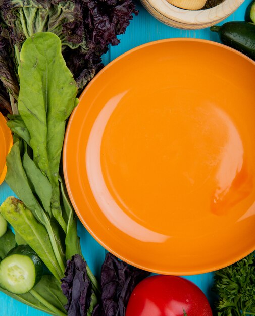 Top view of vegetables as spinach basil cucumber tomato with plate on blue surface