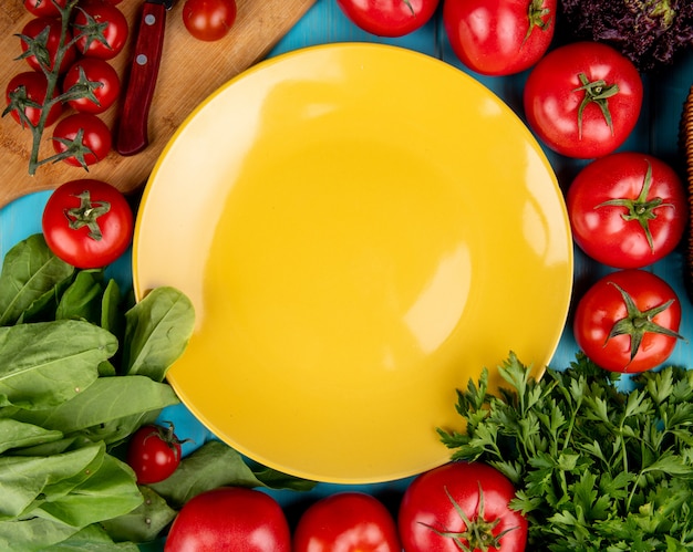 Free Photo top view of vegetables as spinach basil tomato coriander with knife on cutting board and empty plate on blue surface