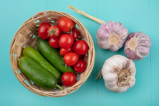 Top view of vegetables as tomato cucumber in basket and garlic on blue surface