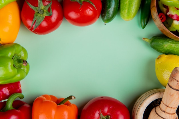 Top view of vegetables as tomato cucumber pepper with lemon and black pepper in garlic crusher on green with copy space