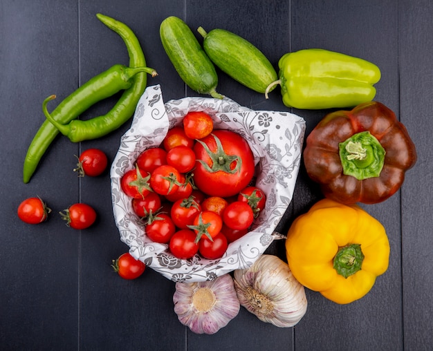 Free photo top view of vegetables as tomatoes in basket cucumbers peppers garlic bulbs on black surface