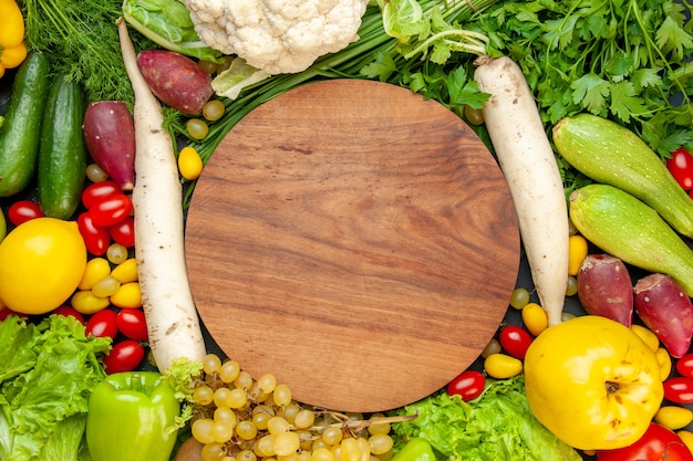 Free Photo top view vegetables and fruits cherry tomatoes cumcuat lettuce quince grape lemon cauliflower white radish parsley zucchini cucumbers round wood board in center